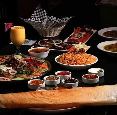 Table spread with a rolled dosa, biryani, fried chicken platters, curries and a mango drink